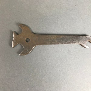 May include: A silver metal wrench with three prongs and a hole in the center.