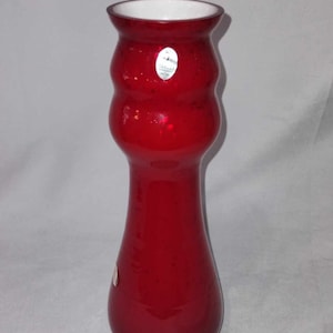 May include: A tall, red glass vase with a white rim and a slightly flared opening. The vase has a textured, bubbly surface and a rounded, bulbous shape.
