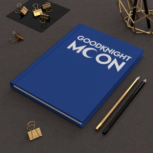 Może przedstawiać: Niebieski notes z napisem "GOODNIGHT MOON" białymi literami. Notes leży na szarej, teksturowanej powierzchni z dwoma ołówkami i złotym, ozdobnym stojakiem metalowym.