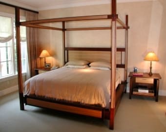 May include: A wooden canopy bed frame with a light brown finish. The bed has a headboard and footboard with a simple design. The bed is made of solid wood and has a sturdy construction.