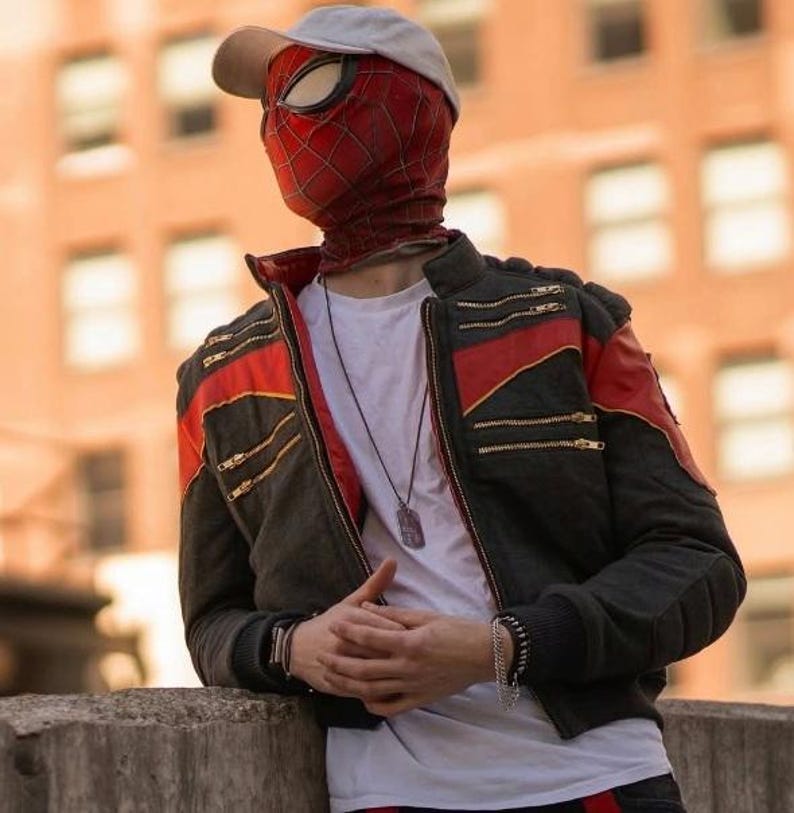 May include: A red and black Spider-Man mask with a white baseball cap, worn with a black jacket featuring red shoulder stripes and gold zippers over a white t-shirt. A silver dog tag necklace and a black beaded bracelet are visible on the chest and wrist.