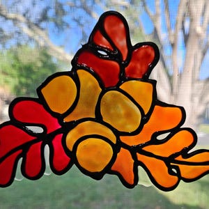 May include: A stained glass design featuring a cluster of leaves in shades of red, orange, and yellow. The leaves are outlined in black and have a glossy finish.