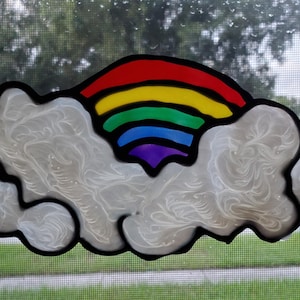 May include: A stained glass window decoration featuring a rainbow arch over a white cloud. The rainbow is made of red, orange, yellow, green, blue, indigo, and violet glass.