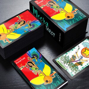 May include: A black box with the text "Meera Tarot" on the front. The box contains a deck of tarot cards with colourful illustrations. The cards feature a variety of characters and symbols, including a woman playing a musical instrument.
