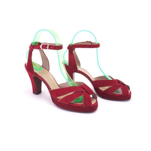 May include: A pair of deep red suede high-heeled sandals featuring a crisscross strap design at the toe, a platform sole, and an adjustable ankle strap with a silver-toned metal buckle. The shoes have a sturdy block heel and a rounded toe.