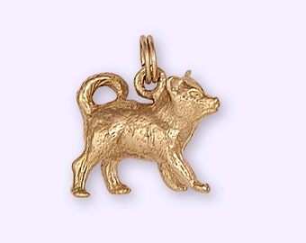 Könnte beinhalten: Ein goldfarbener Anhänger in Form eines kleinen Hundes. Der Hund steht auf allen vieren und hat den Kopf zur Seite gedreht. Der Anhänger ist aus Metall und hat eine glänzende Oberfläche.