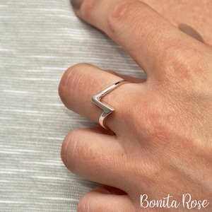 May include: A silver ring with a geometric V-shaped design. The ring is worn on a finger.