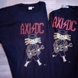 May include: Two black t-shirts featuring a graphic of an axolotl playing a guitar and the text "AXI/DC" printed in red.