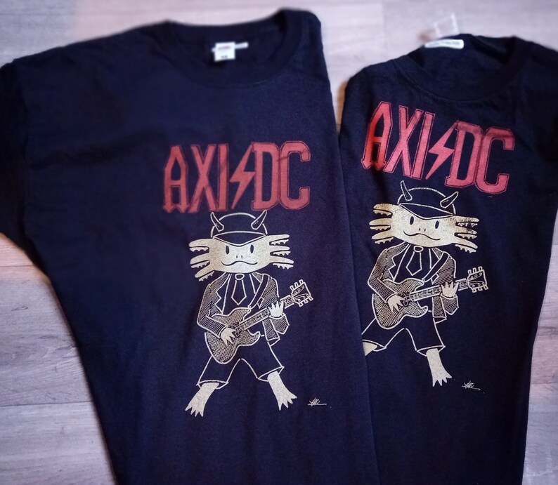 May include: Two black t-shirts featuring a graphic of an axolotl playing a guitar and the text "AXI/DC" printed in red.