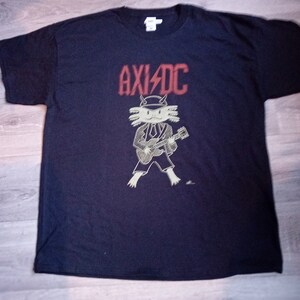 May include: A black t-shirt featuring a red "AXID"C logo and a cartoon axolotl playing a guitar.