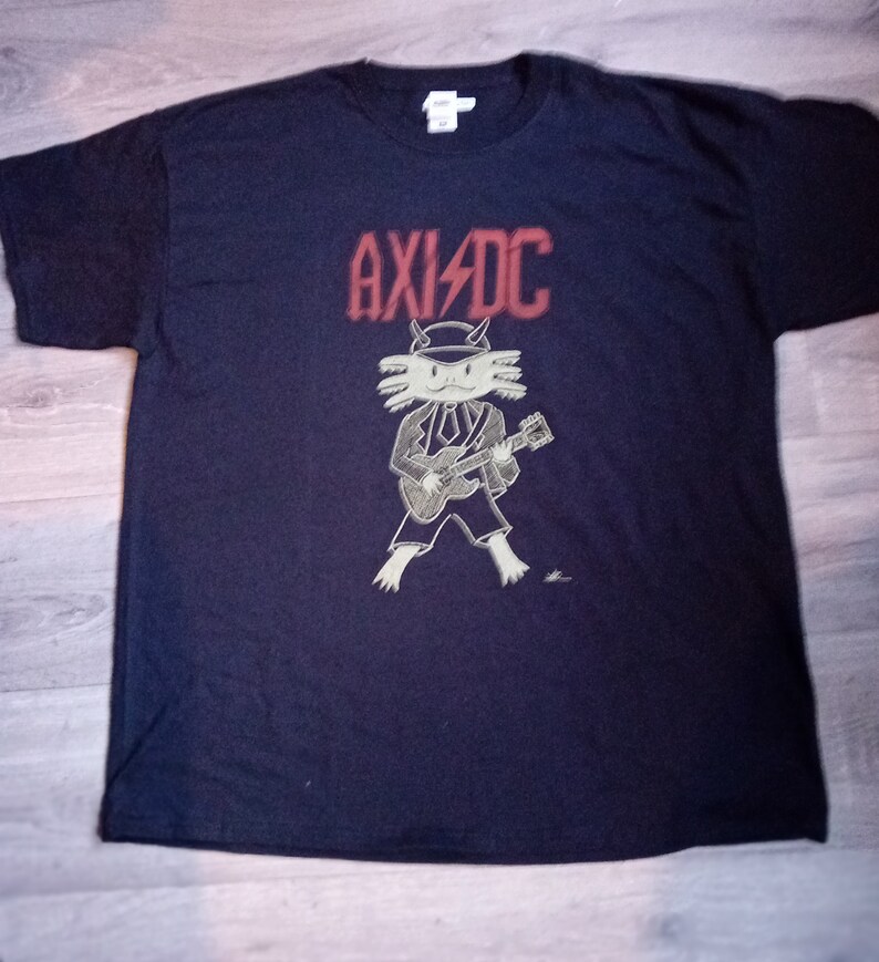 May include: A black t-shirt featuring a red "AXID"C logo and a cartoon axolotl playing a guitar.