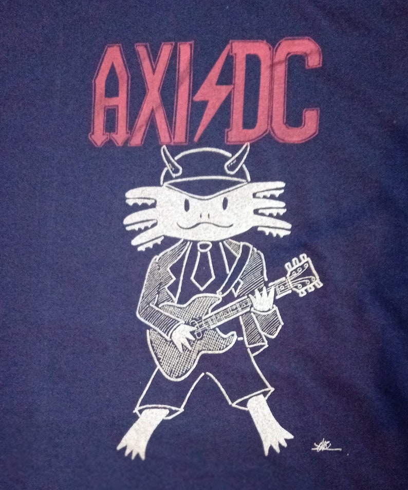 May include: A blue t-shirt featuring a white axolotl wearing a suit and playing a guitar. The text "AXI/DC" is printed in red above the axolotl.