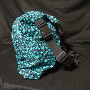May include: A teal and black patterned fanny pack with a repeating bird design. The bag has a black adjustable strap with a plastic buckle. A teal zip runs along the top of the bag.