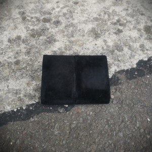 K&ouml;nnte beinhalten: Ein schwarzes rechteckiges St&uuml;ck Stoff mit glatter Textur. Der Stoff ist in der Mitte gefaltet und scheint aus einem weichen Material zu bestehen.