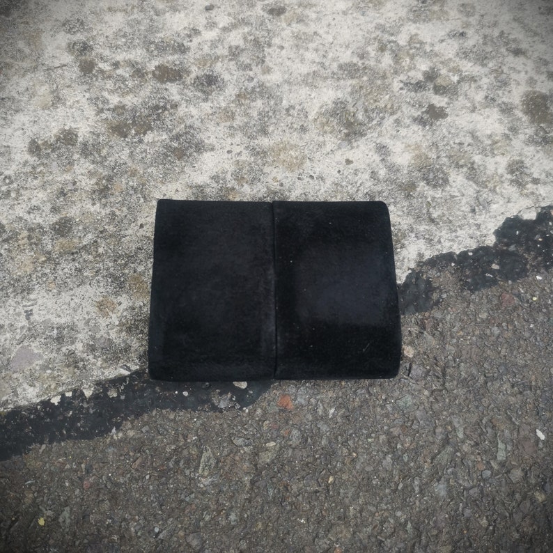 K&ouml;nnte beinhalten: Ein schwarzes rechteckiges St&uuml;ck Stoff mit glatter Textur. Der Stoff ist in der Mitte gefaltet und scheint aus einem weichen Material zu bestehen.