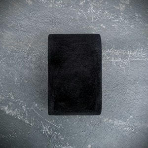 K&ouml;nnte beinhalten: Ein schwarzes rechteckiges Objekt mit einer glatten, leicht strukturierten Oberfl&auml;che. Das Objekt liegt auf einer grauen, strukturierten Oberfl&auml;che.