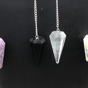 May include: Four crystal pendulums with silver chains. The pendulums are amethyst, black obsidian, clear quartz, and white howlite.