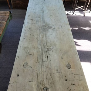 Puede incluir: Una mesa de madera clara y desgastada con nudos y vetas visibles. La superficie muestra signos de desgaste y uso, con arañazos y marcas.