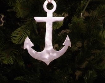 May include: A white metal anchor ornament hanging from a brown twine string on a green Christmas tree.