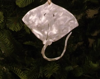 May include: A white ceramic ornament shaped like a stingray with a brown string for hanging. The stingray has a black face with two eyes and a mouth.