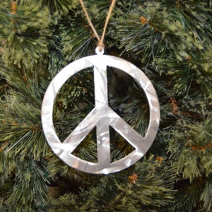 Può includere: Un ornamento a forma di segno della pace argentato appeso a un albero di Natale verde.