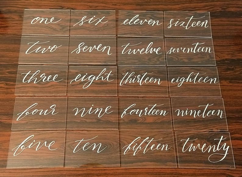 May include: Twenty clear acrylic table number cards with white calligraphy. The numbers one through twenty are written in cursive.