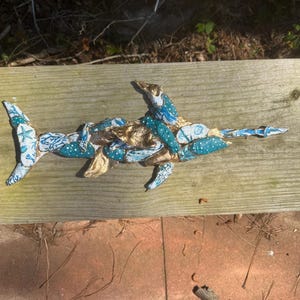May include: A handcrafted shark sculpture made from fabric and gold-colored material. The shark features blue and white patterned fabric with starfish and polka dots. The sculpture is placed on a wooden surface.