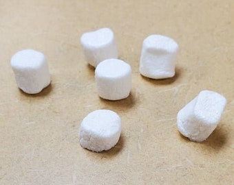 Può includere: Un gruppo di sette marshmallow bianchi su una superficie beige.