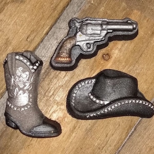May include: A set of three black and silver cowboy-themed cake toppers. The set includes a cowboy hat, a boot, and a revolver.
