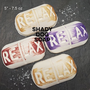 May include: Four white rectangular soaps with the word "RELAX" embossed on them. The text is painted in gold, burgundy, and purple. The soaps are approximately 5 inches long and weigh 7.5 oz. The brand name "SHADY DOG SOAP" is also visible.