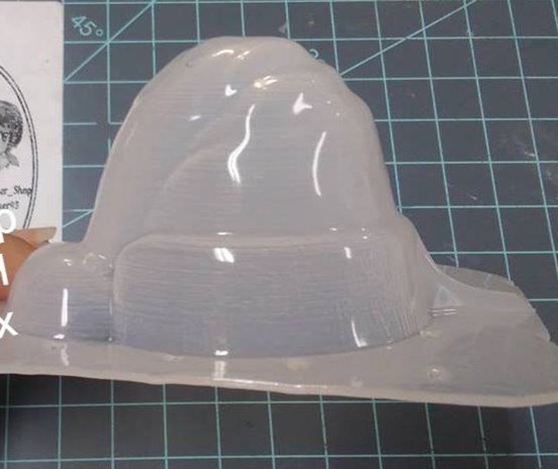 Op de afbeelding: Een transparante plastic mal in de vorm van een heksenhoed. De mal is ontworpen om een hoed te maken met een brede rand en een hoge, puntige kroon.