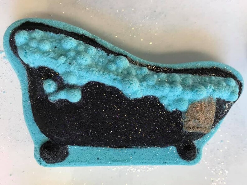 Puede incluir: Una bomba de ba&ntilde;o azul y negra con forma de ba&ntilde;era con una parte superior espumosa. La bomba de ba&ntilde;o est&aacute; cubierta de purpurina.