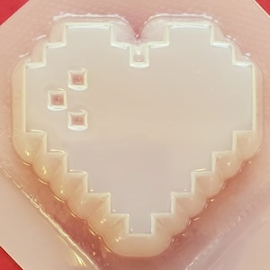 May include: A white silicone mould shaped like a pixelated heart. The mould is designed to create a heart-shaped object with a pixelated design.