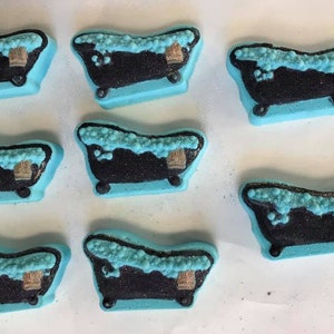 Puede incluir: Ocho bombas de ba&ntilde;o azules con forma de ba&ntilde;era con detalles en blanco y negro. Las bombas de ba&ntilde;o est&aacute;n llenas de espuma blanca y tienen un acento marr&oacute;n.