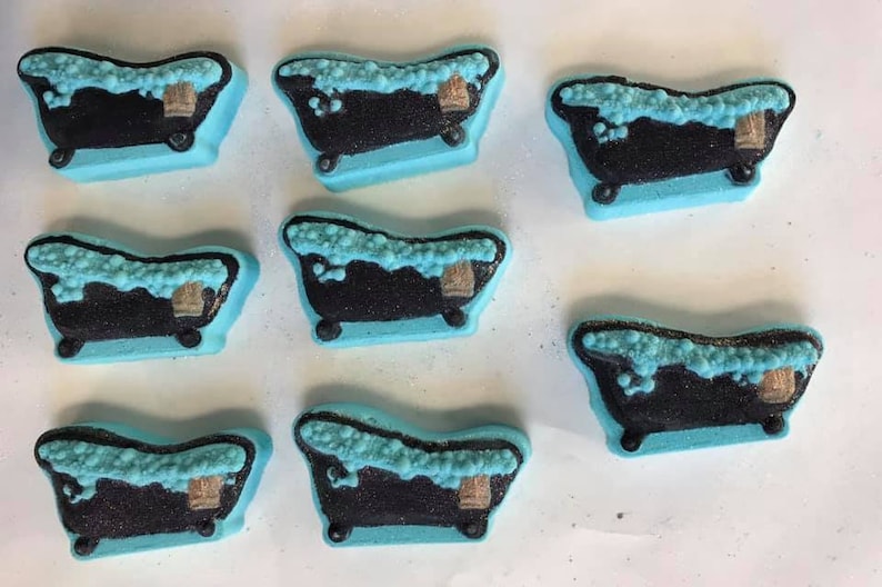 Puede incluir: Ocho bombas de ba&ntilde;o azules con forma de ba&ntilde;era con detalles en blanco y negro. Las bombas de ba&ntilde;o est&aacute;n llenas de espuma blanca y tienen un acento marr&oacute;n.