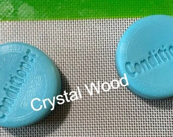 Puede incluir: Dos objetos redondos de color azul claro con la palabra "Conditioner" grabada en la superficie. Los objetos están sobre una superficie de malla gris con un borde verde. También es visible el texto "Crystal Wood".