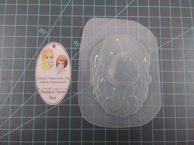 May include: Clear plastic mold of a dog's head, suitable for making soap, candles, or resin crafts. The mold is on a green cutting mat.