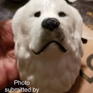 May include: White ceramic dog head sculpture with black painted details. The dog has a fluffy, textured surface and a black nose.