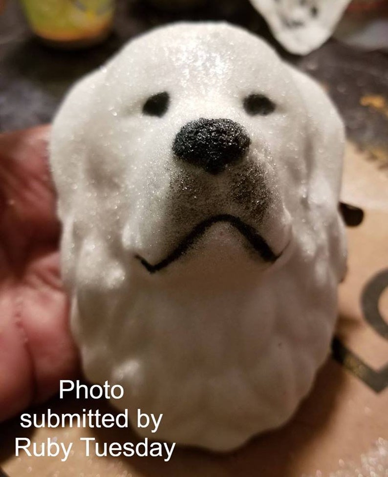 May include: White ceramic dog head sculpture with black painted details. The dog has a fluffy, textured surface and a black nose.