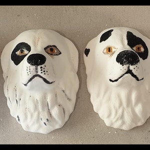 May include: Four ceramic dog head sculptures with black and white markings. The sculptures are painted with brown and orange accents around the eyes and nose.