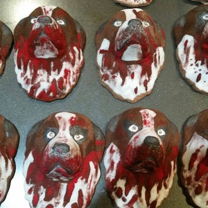 May include: Eight painted dog heads on a baking sheet. The dog heads are brown with white and red paint, resembling blood splatters.