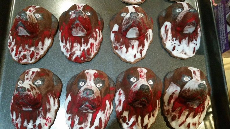 May include: Eight painted dog heads on a baking sheet. The dog heads are brown with white and red paint, resembling blood splatters.