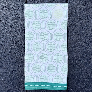 May include: White kitchen towel with a green and white pattern of tennis rackets. The towel has a green border with white dots.