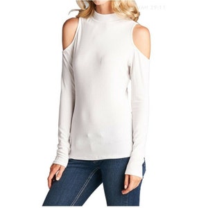 May include: White long-sleeve shirt with a mock neck and cut-out shoulders.
