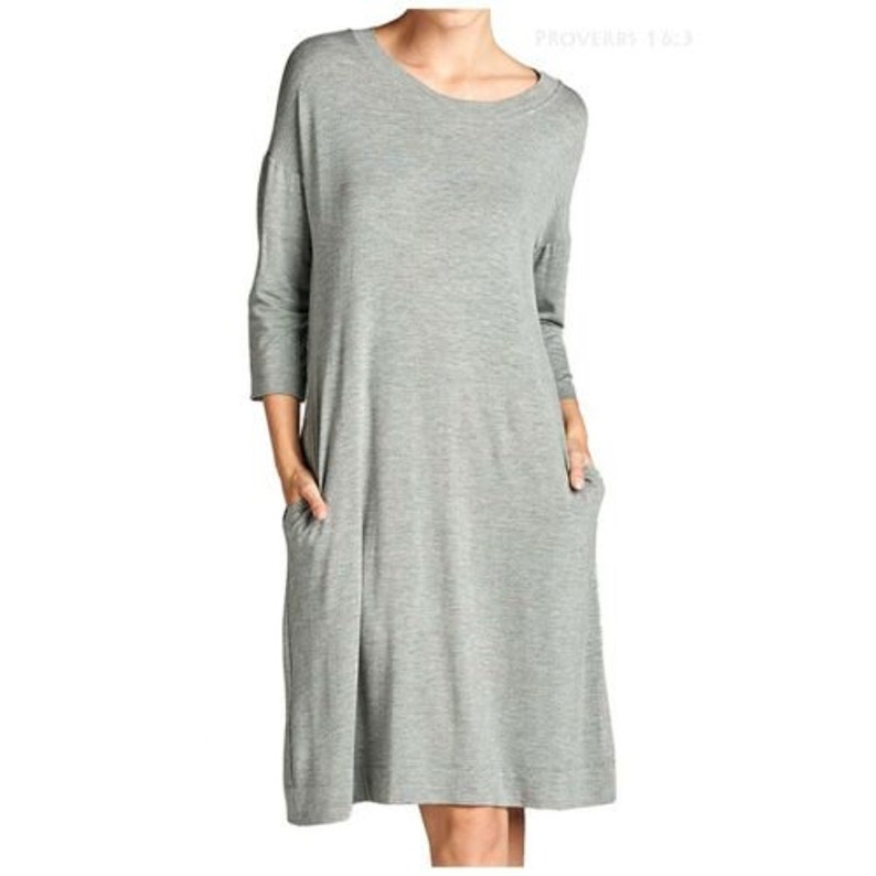 Puede incluir: Un vestido gris, de manga larga, informal, con cuello redondo y dos bolsillos. El vestido est&aacute; hecho de una tela suave y c&oacute;moda.