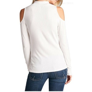 May include: White long-sleeve shirt with a mock neck and cold shoulder cutouts. The shirt is made of a soft, stretchy fabric.