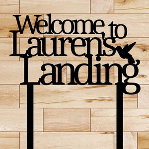 Puede incluir: Se&ntilde;al de metal negro con el texto "Bienvenido a Lauren's Landing" y una silueta de colibr&iacute;. La se&ntilde;al est&aacute; montada en dos estacas de metal negro.