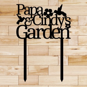 Puede incluir: Estaca de jard&iacute;n de metal negro con el texto "Papa & Cindy's Garden" y dos colibr&iacute;es y flores.