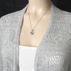 May include: A silver necklace with a spiral pendant. The necklace is on a mannequin wearing a gray cardigan.