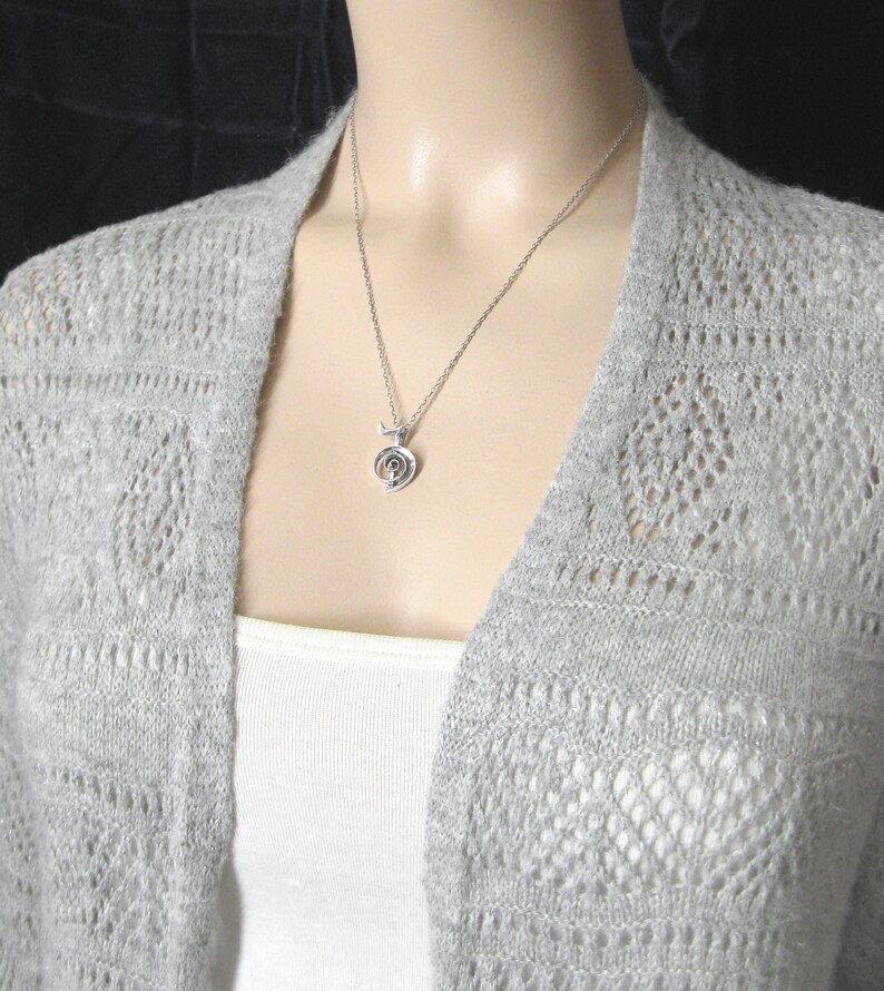May include: A silver necklace with a spiral pendant. The necklace is on a mannequin wearing a gray cardigan.